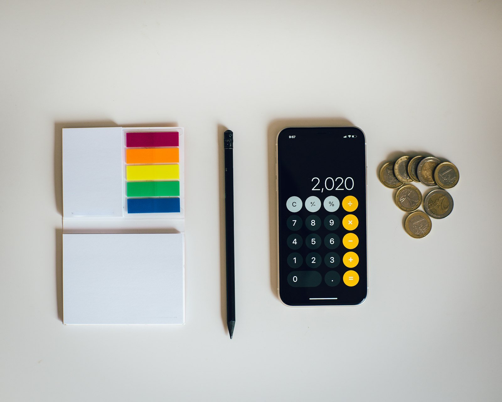 Phone calculator next to a notepad, a pen and a stack of coins, working out a budget