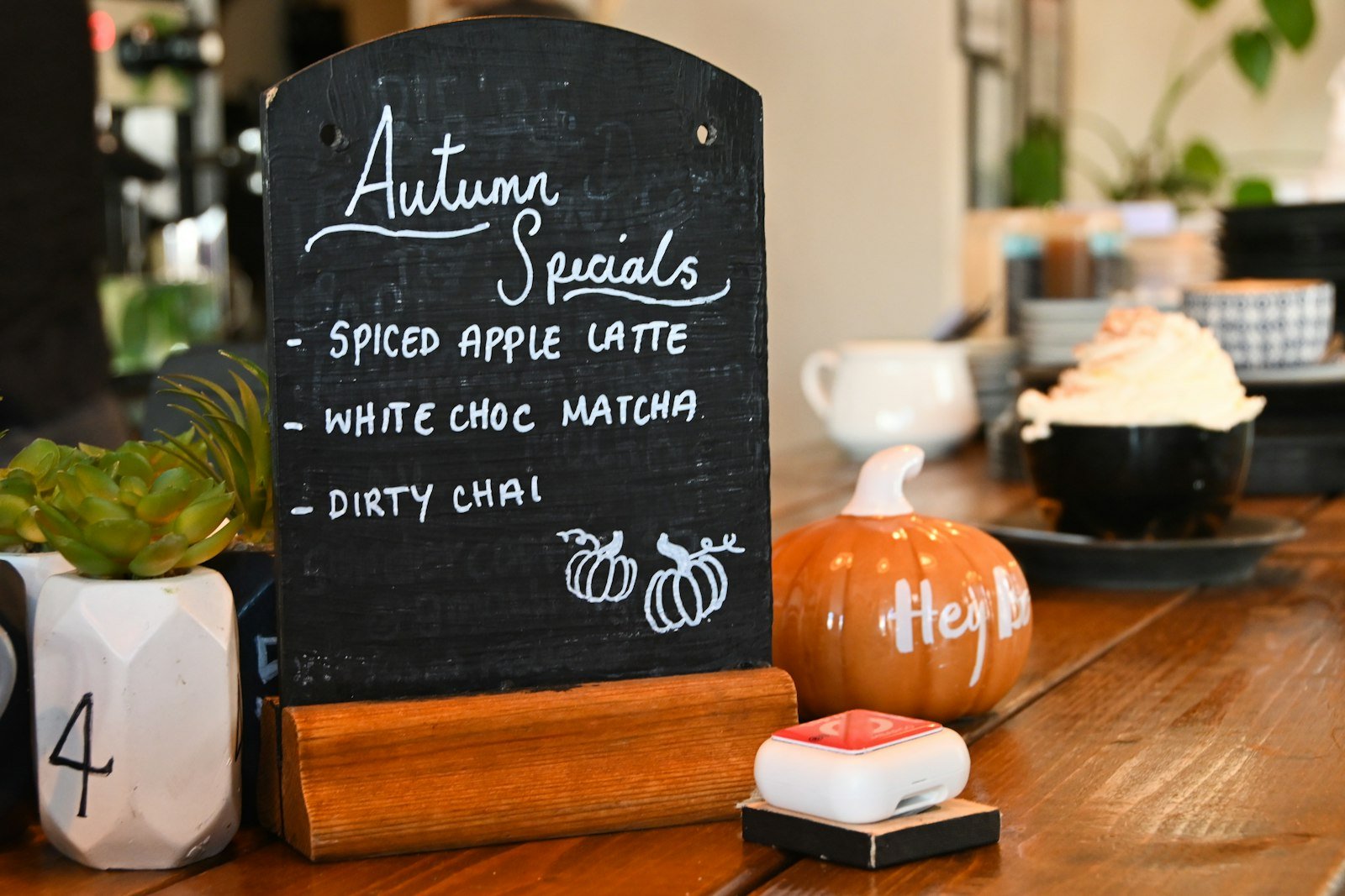 Cafe counter chalkboard listing autumn specials beside a small pumpkin
