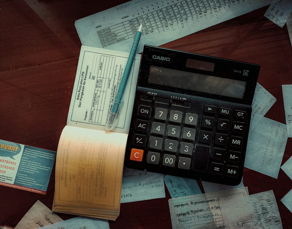 Calculator and pen lying on receipts and a cheque book on a wooden table