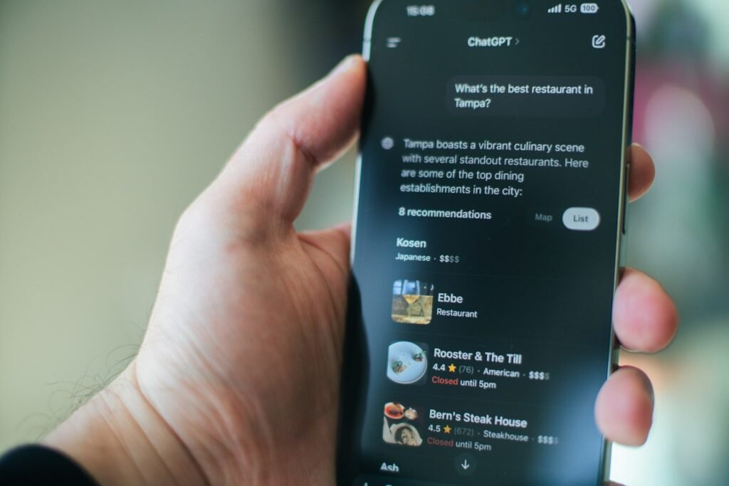 Hand holding a phone where ChatGPT answers "What's the best restaurant in Tampa?" with a list of named restaurants and ratings