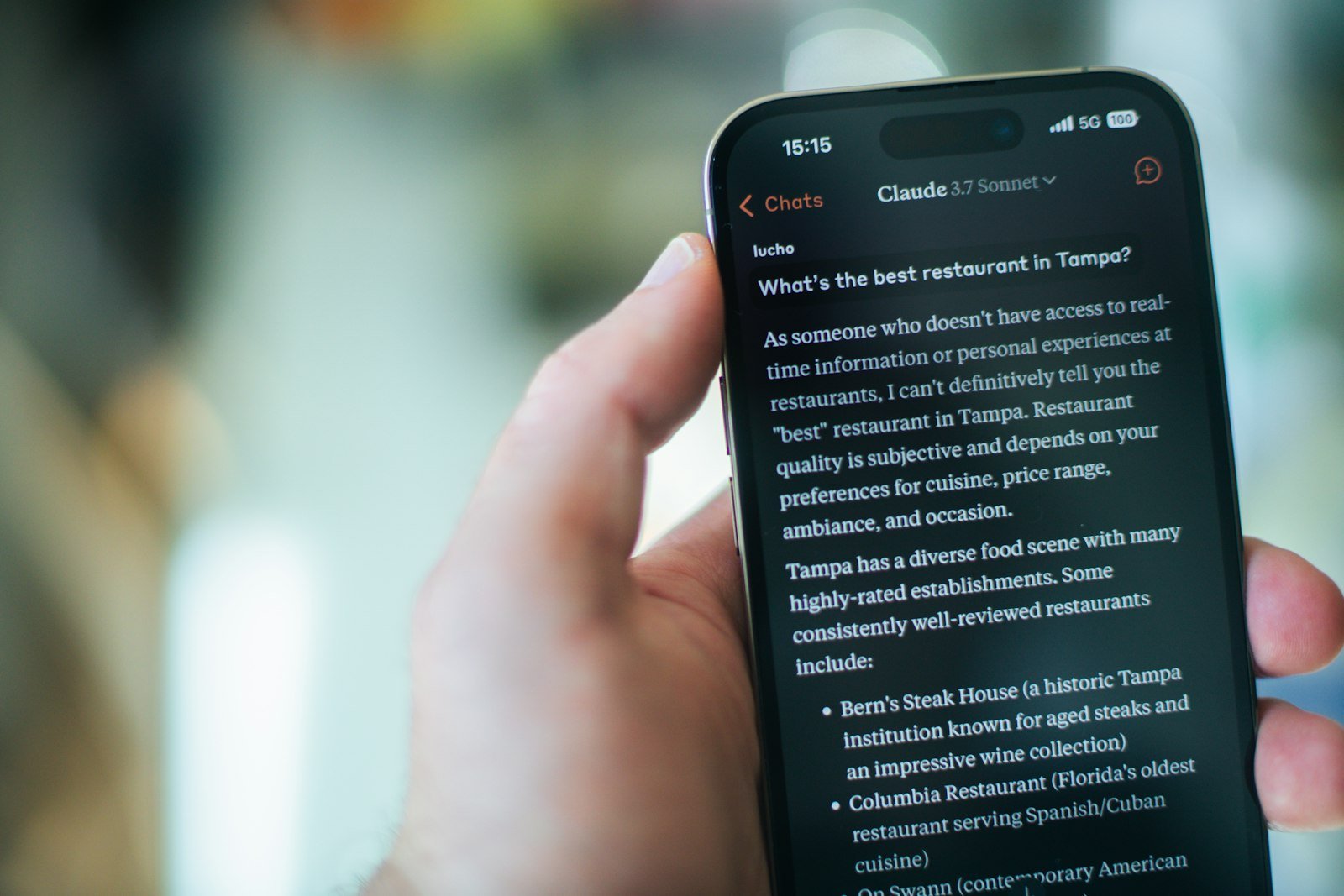 Hand holding a phone showing a Claude chat with a written answer