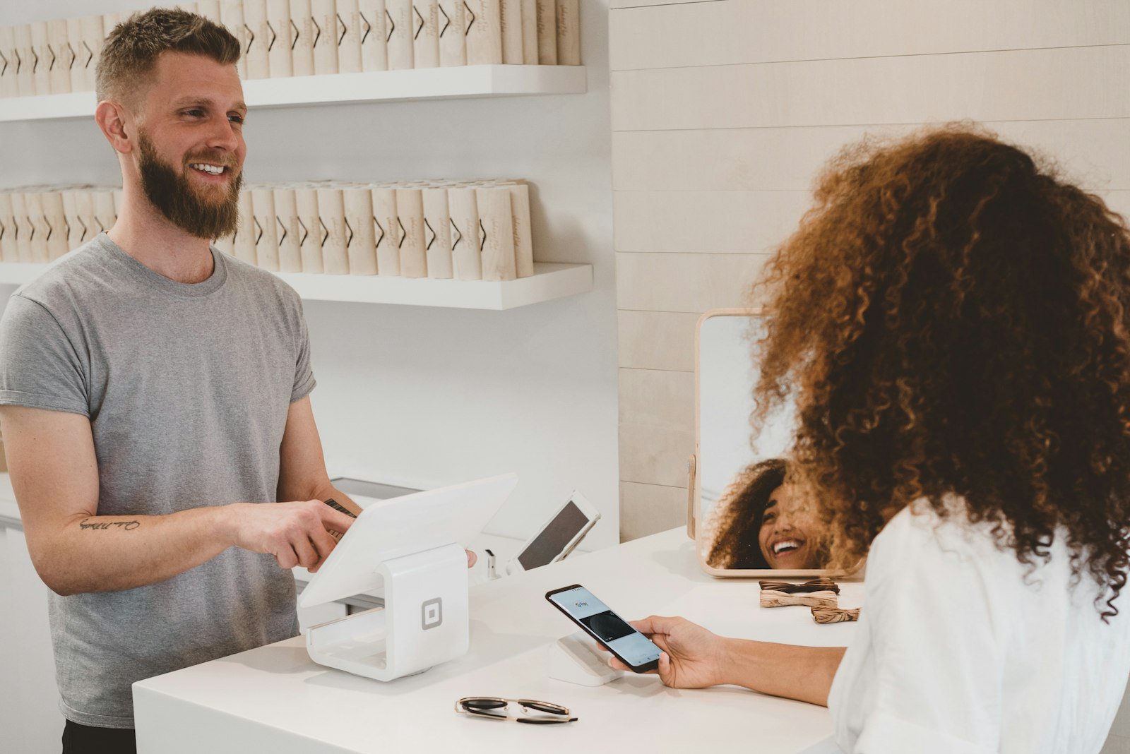 Shop owner smiling at a customer paying with a phone at the counter