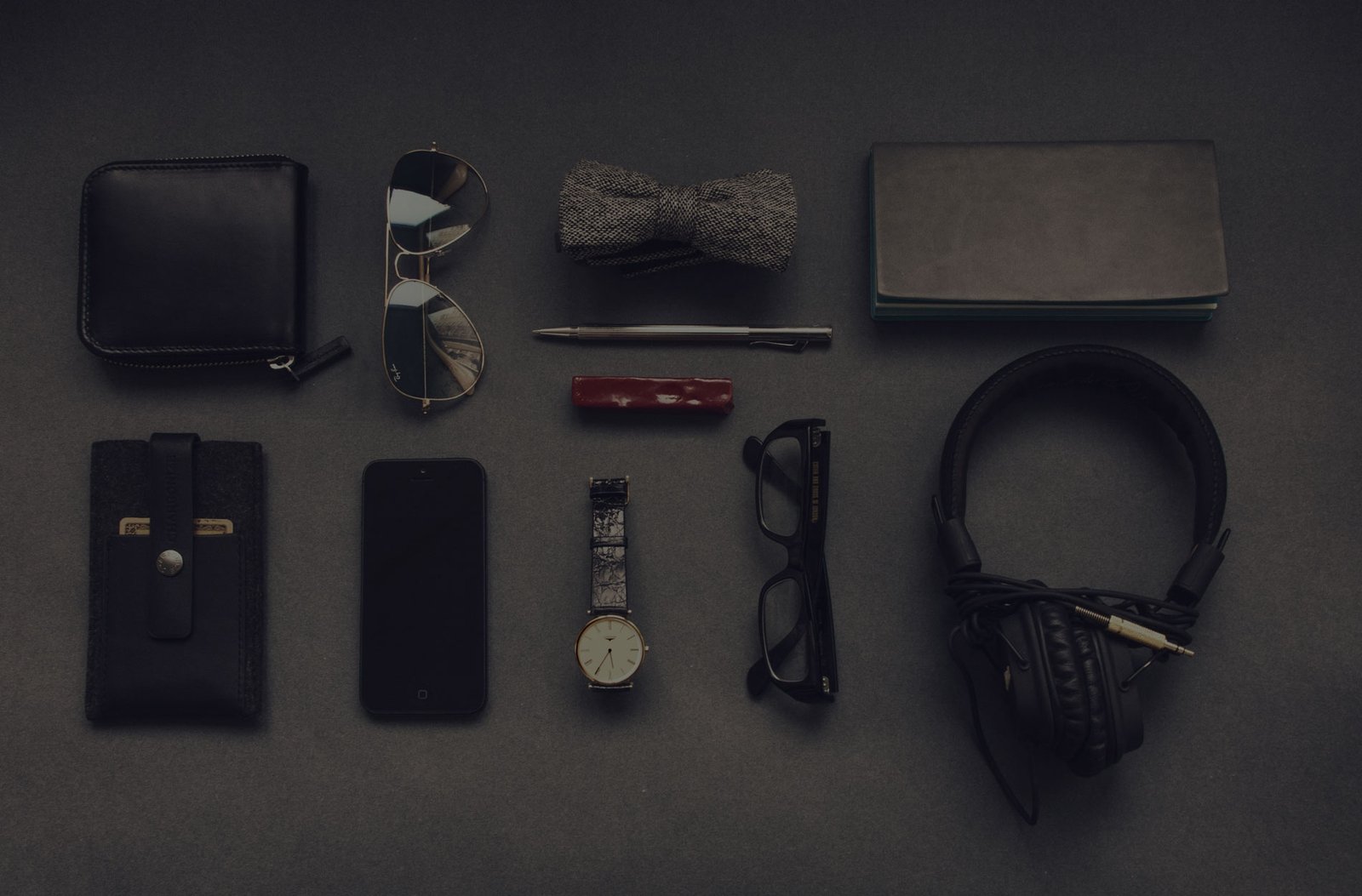 Phone, notebook, glasses and headphones laid out on a dark desk