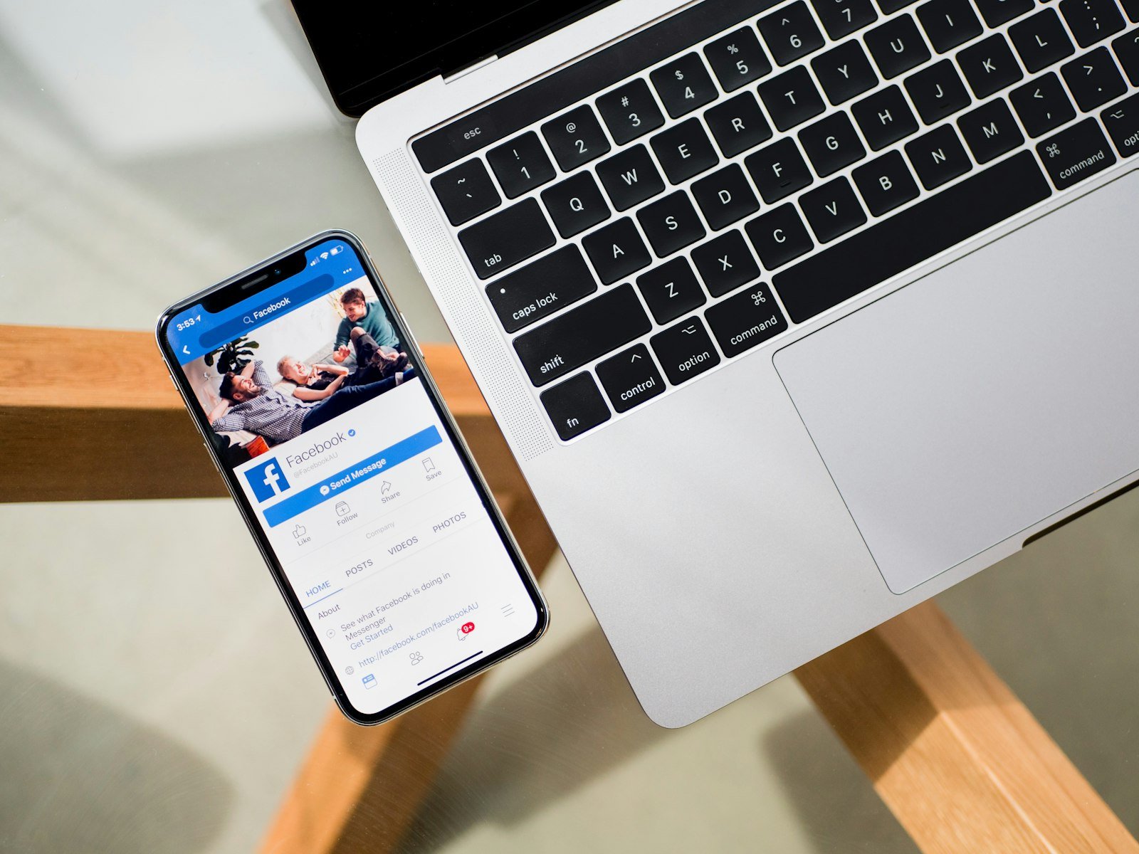Phone showing a Facebook page, resting beside a laptop keyboard