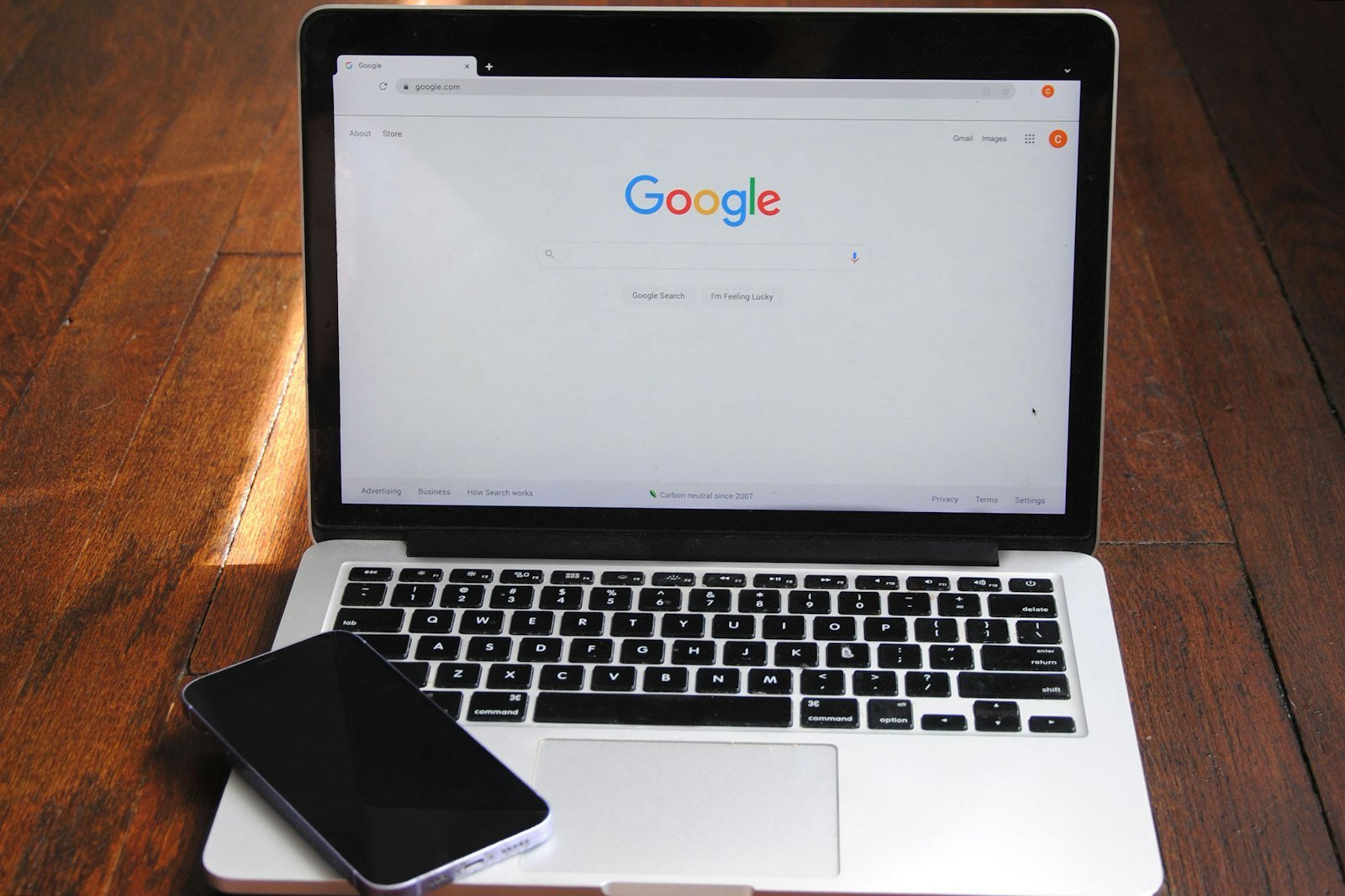 A laptop on a wooden desk showing the Google search home page