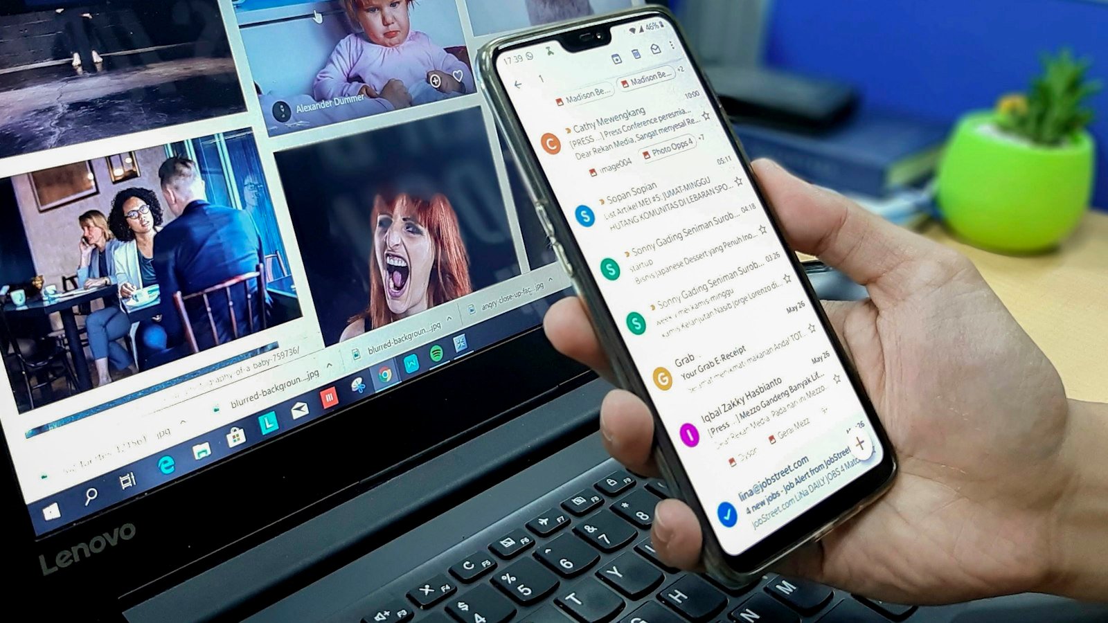 A phone showing an email inbox held in front of a laptop