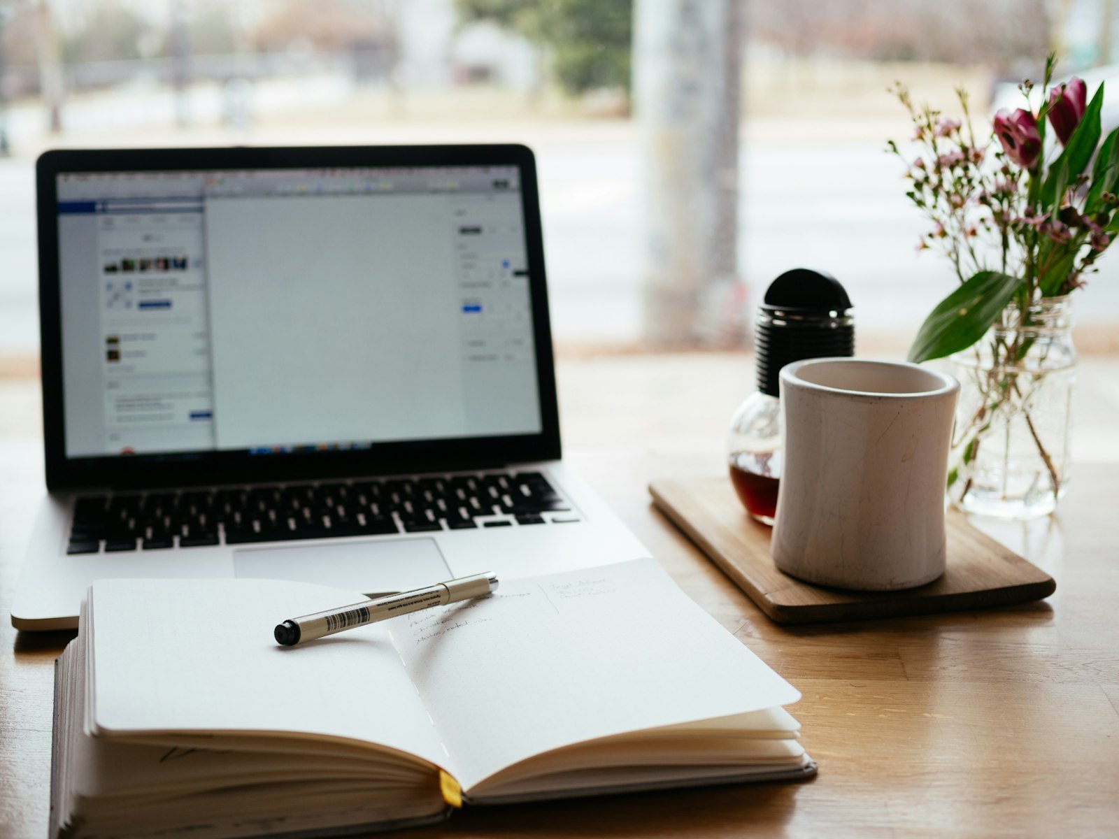 A laptop beside an open notebook and a cup of coffee on a desk