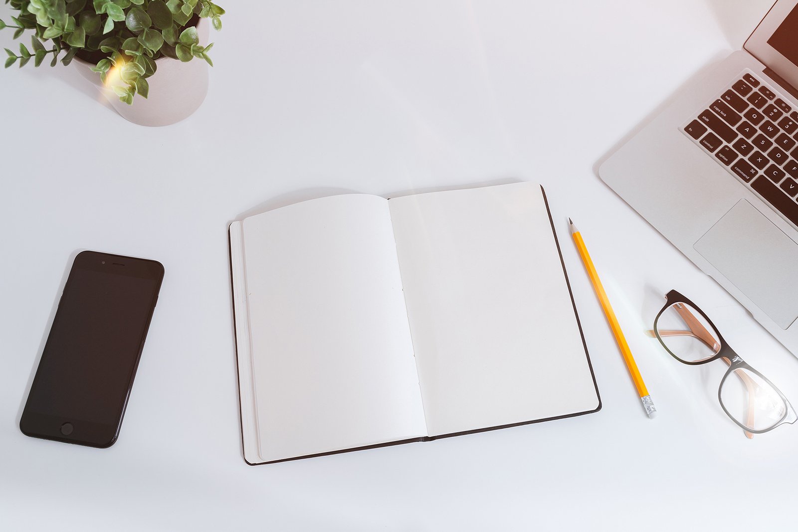 An open notebook, phone and laptop on a desk while outlining an article
