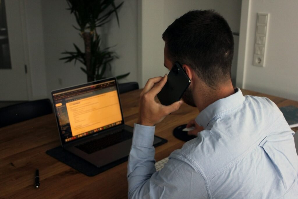 A man returning a call from his desk with a laptop open in front of him