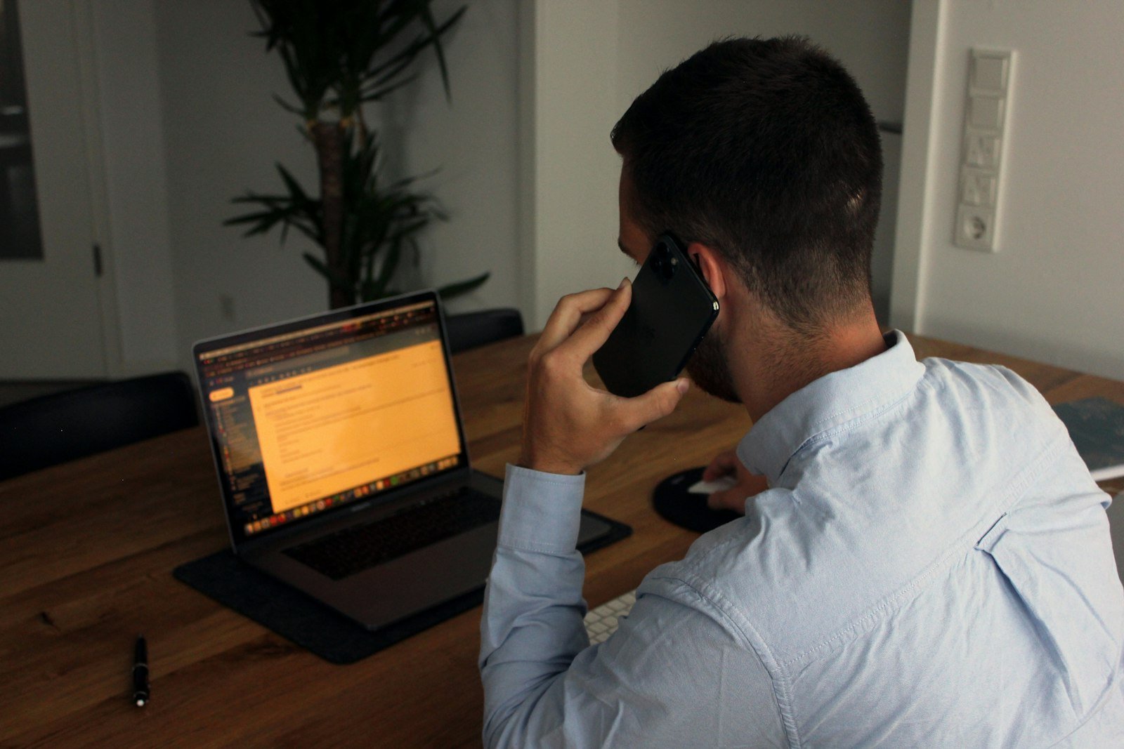 A man returning a call from his desk with a laptop open in front of him