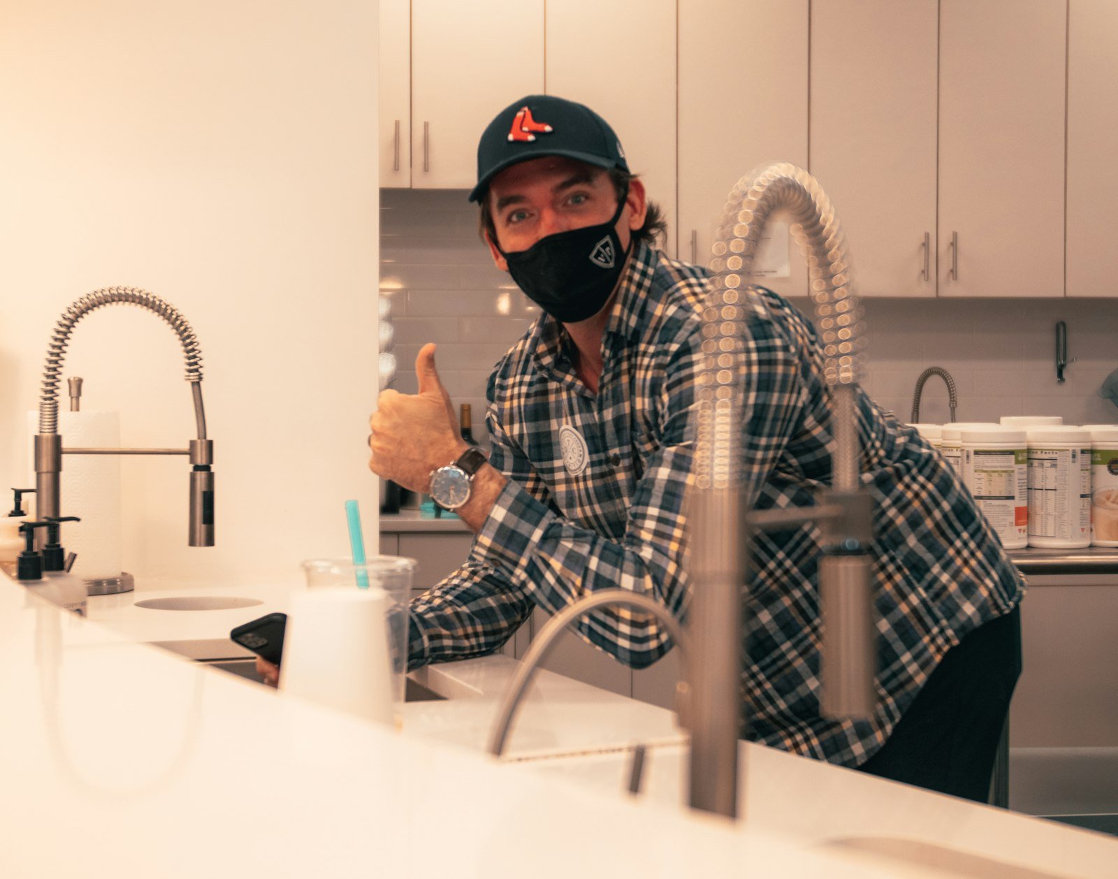 Tradesperson in a cap and face mask giving a thumbs-up beside a kitchen tap