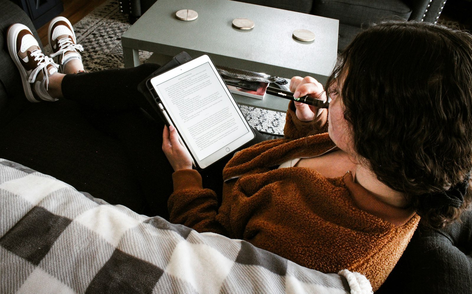 Woman relaxing on a couch reading a document on a tablet, with a laptop beside her
