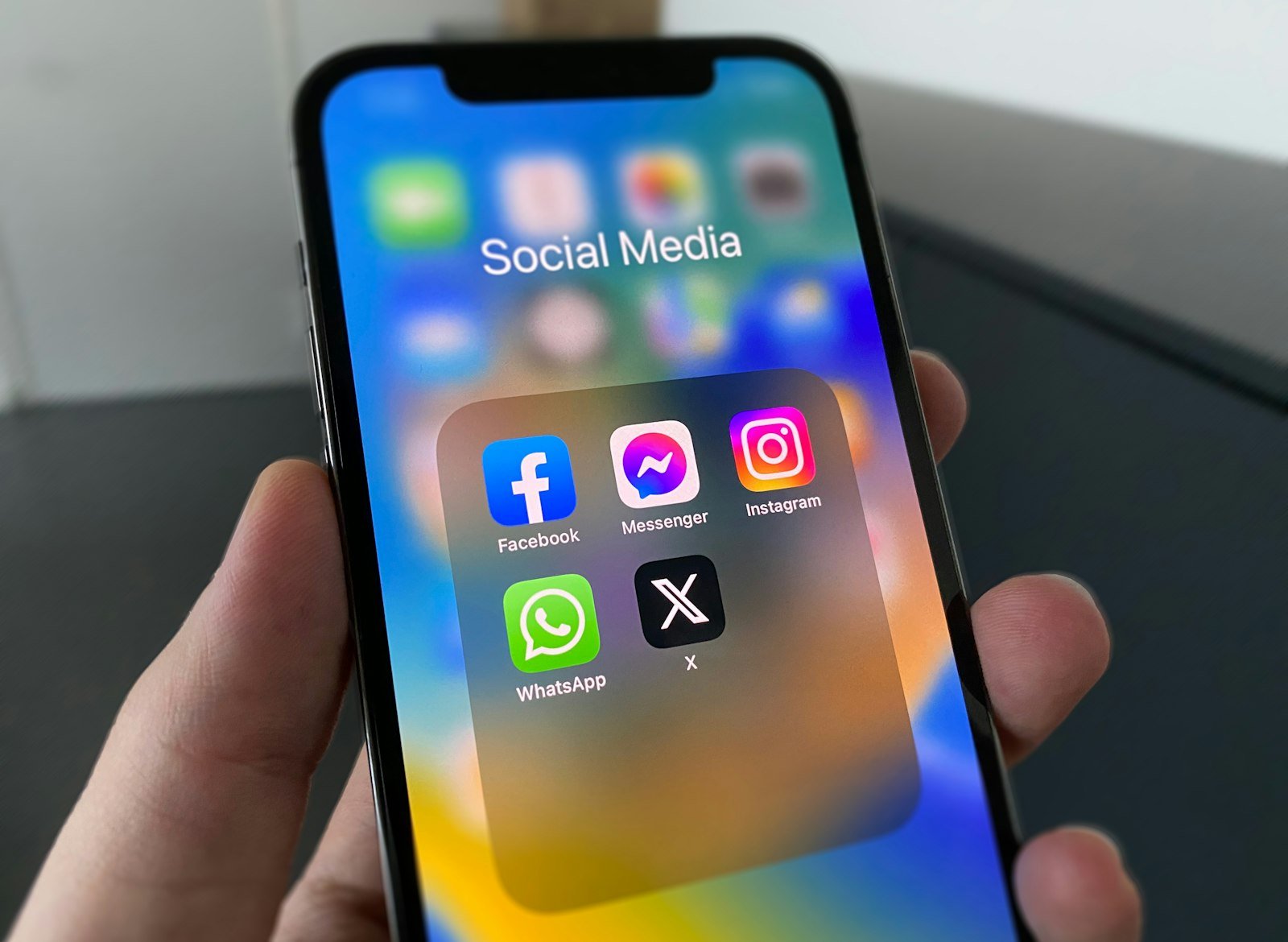 A hand holding a phone with a folder of social media apps open