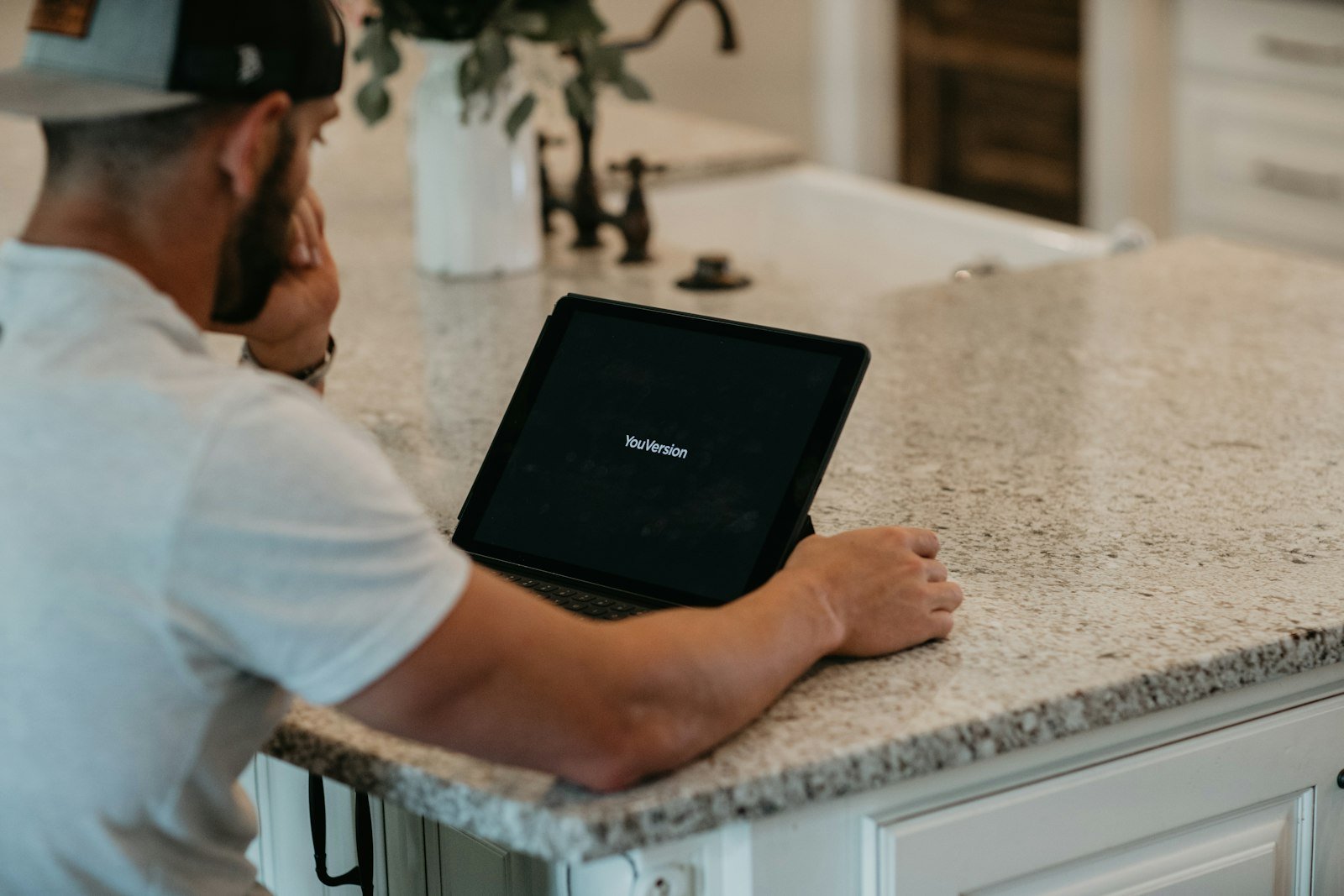 Man in a cap using a tablet at a kitchen counter